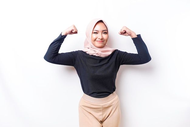 Excited Asian Muslim woman wearing a hijab showing strong gesture by lifting her arms and muscles smiling proudly