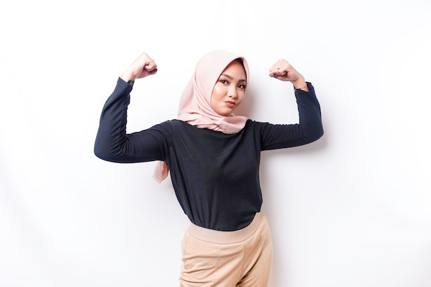 Excited Asian Muslim woman wearing a hijab showing strong gesture by lifting her arms and muscles smiling proudly