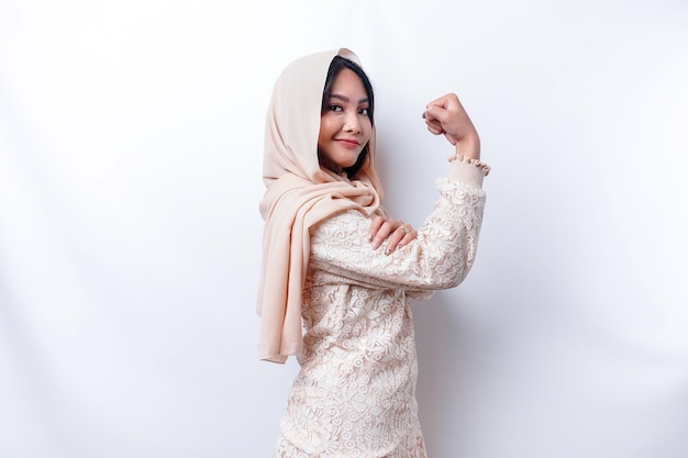 히잡을 쓴 흥분한 아시아 무슬림 여성은 팔과 근육을 자랑스럽게 들어 올려 강한 몸짓을 보여줍니다