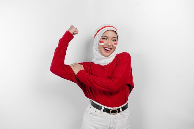 Excited Asian muslim woman wearing a red top and white hijab showing strong gesture by lifting her arms and muscles smiling proudly Indonesia's independence day concept