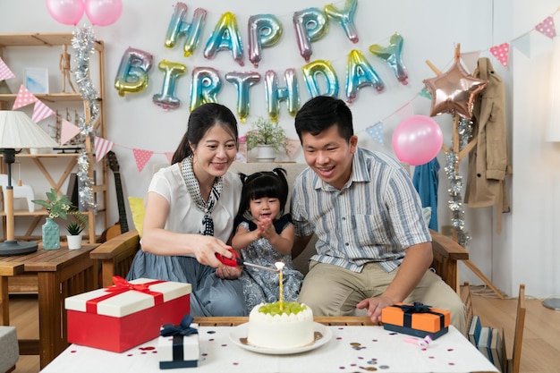 excited asian toddler baby girl clapping hands as her mother is lighting birthday candle on the cake during birthday celebration at home