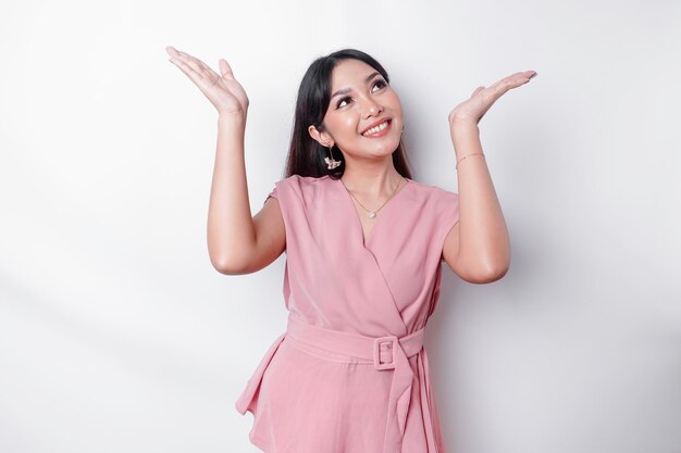 Excited Asian woman dressed in pink pointing at the copy space on top of her isolated by white background