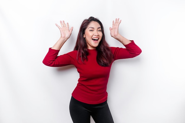 Excited Asian woman dressed in red pointing at the copy space on top of her isolated by white background