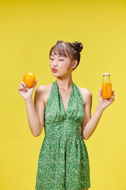 Excited asian woman drinking beverage freshness orange juice glass standing on yellow background