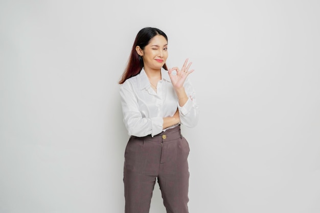 Excited Asian woman giving an OK hand gesture isolated by a white background