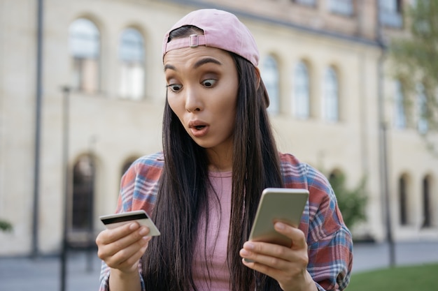 Excited asian woman holding credit card shopping online on her smart phone