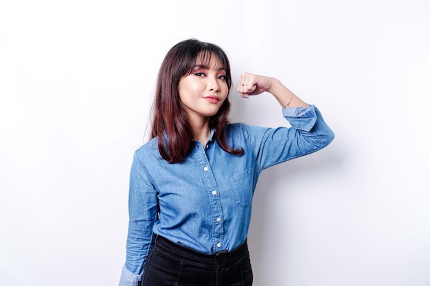 Excited Asian woman wearing a blue shirt showing strong gesture by lifting her arms and muscles smiling proudly