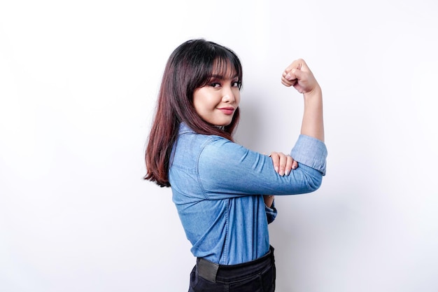 Excited Asian woman wearing a blue shirt showing strong gesture by lifting her arms and muscles smiling proudly