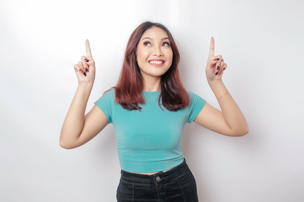 Donna asiatica eccitata che indossa una maglietta blu che punta allo spazio della copia sopra di lei isolato da sfondo bianco
