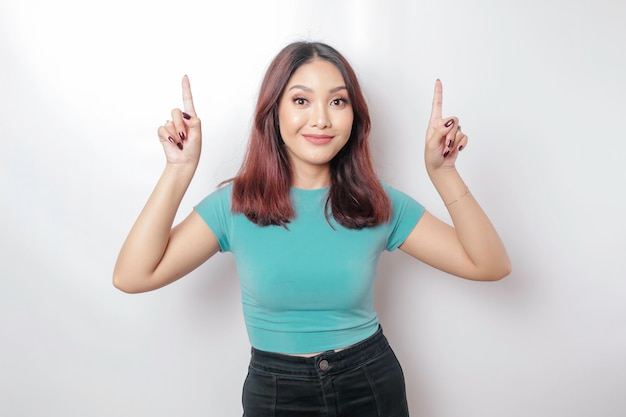 Excited Asian woman wearing blue tshirt pointing at the copy space on top of her isolated by white background