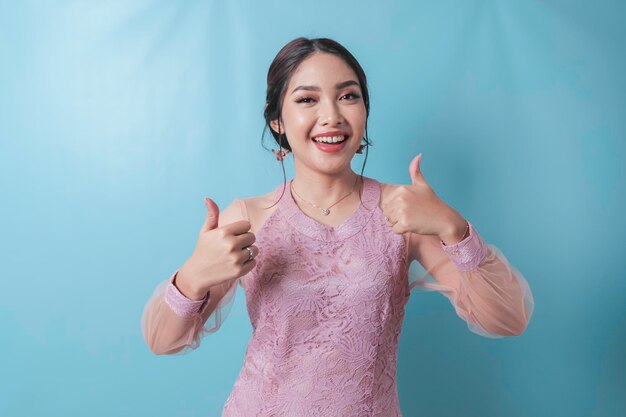 Возбужденная азиатка в современной одежде кебайя показывает большой палец вверх жестом руки