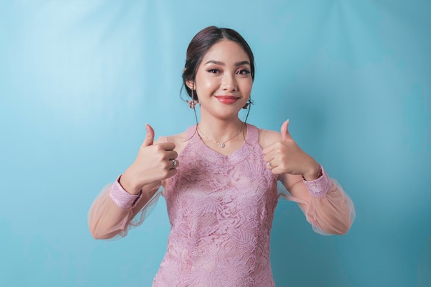 Excited Asian woman wearing modern kebaya clothes giving thumbs up hand gesture