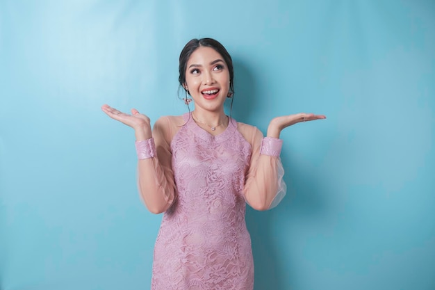 Excited Asian woman wearing modern kebaya clothes pointing at the copy space upwards