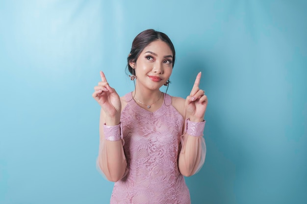 Excited asian woman wearing modern kebaya clothes pointing at the copy space upwards