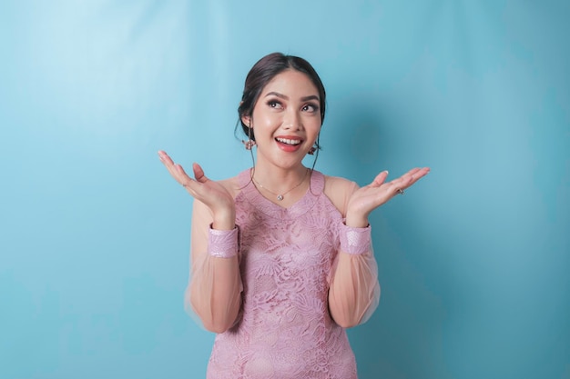 Excited Asian woman wearing modern kebaya clothes pointing at the copy space upwards