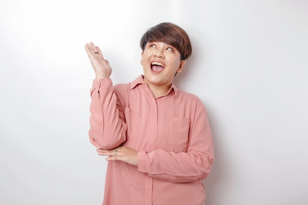 Excited Asian woman wearing pink shirt pointing at the copy space upside her isolated by white background