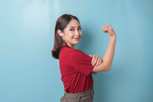 Взволнованная азиатка в красной футболке показывает сильный жест, поднимая руки и гордо улыбаясь