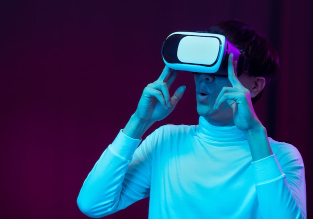 Excited asian young man wearing VR headset in neon light, Future technology concept.