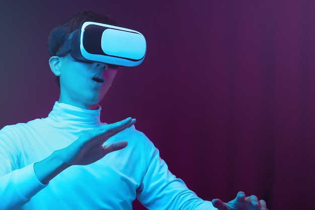 Excited asian young man wearing VR headset in neon light, Future technology concept.