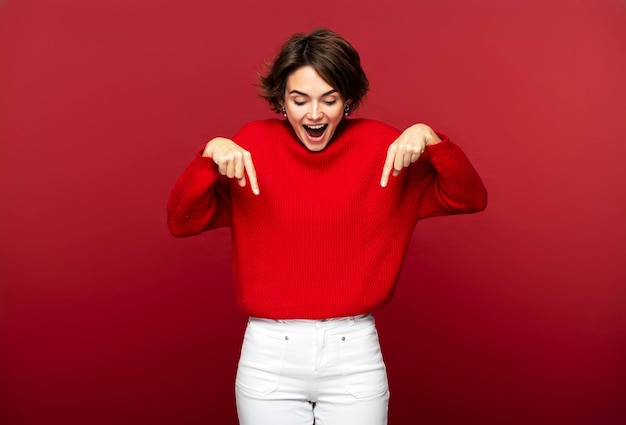 Excited attractive woman pointing down with her forefingers isolated on a red background