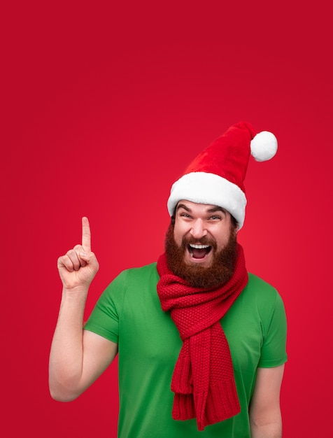 Excited bearded guy in Christmas hat pointing up