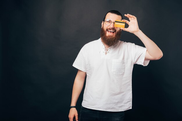 Excited bearded man is covering one eye with a credit card.