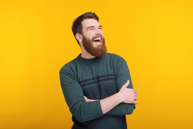 Excited bearded man is laughing with arms crossed on yellow.