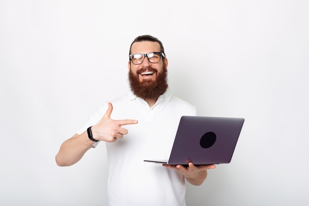 Excited bearded man is pointing at his laptop over white background.