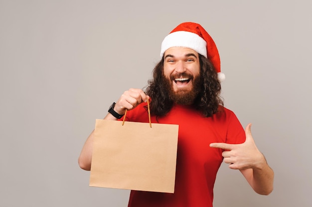 興奮したひげを生やした男は、彼が持っているクラフト ショッピング バッグを指しています。