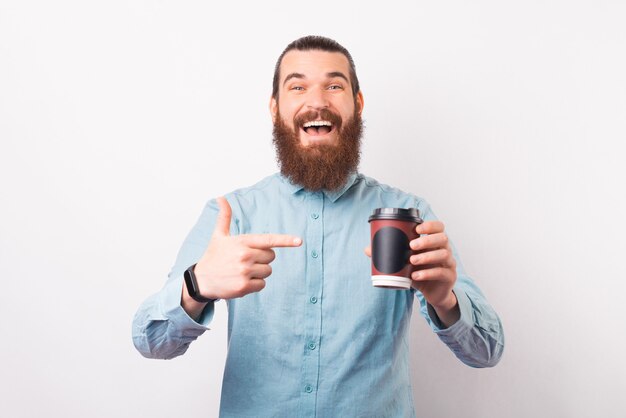 Excited bearded man is pointing at a paper cup of coffee he is holding.