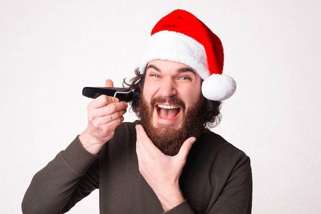 Excited bearded man, new shaver discounts demonstration, wearing a red santa hat