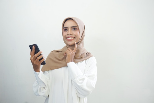 Excited beautiful Asian muslim woman showing mobile phone isolated over white background