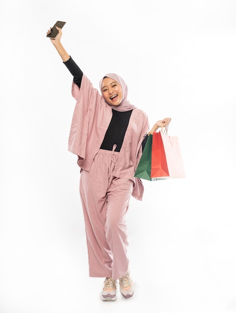 Excited beautiful asian muslim woman with hijab raise her arm while holding shopping bag