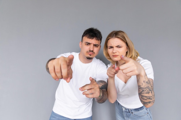 Excited beautiful couple wearing white tshirts standing isolated over gray background pointing at