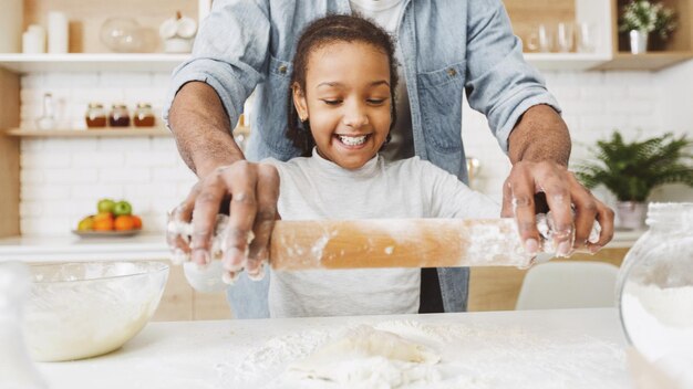 Ragazza nera eccitata che rotola la pasta sotto la supervisione di papà