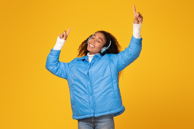 Excited black lady dances in headphones yellow background