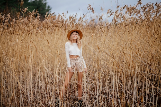 Excited blonde happy safari style girl in a straw hat walks on nature among the reeds.