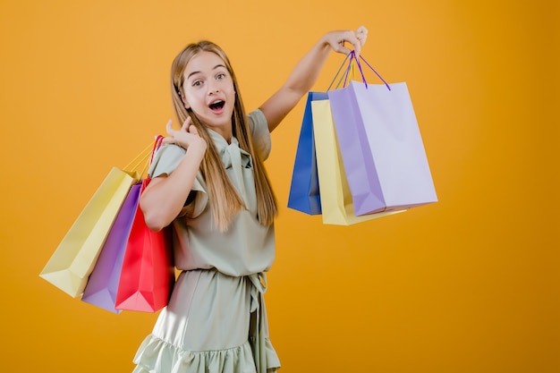 Excited blonde woman with colorful shopping bags isolated over yellow