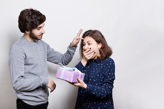 excited brunette holding a present in her hands being surprised to receive it. careful hipster giving a present to his girlfriend and smoothing her hair gently. Smiling couple with present