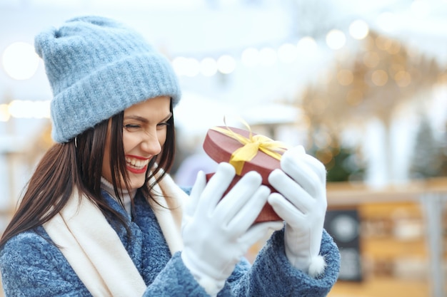 クリスマスフェアでギフトボックスを保持している冬のコートで興奮したブルネットの女性。テキスト用のスペース