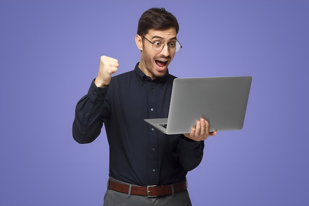 Excited business man looking at laptop screen with mouth wide open celebrating his win