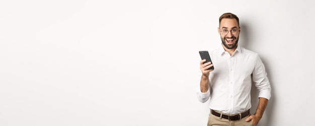Взволнованный деловой человек, использующий мобильный телефон, выглядит пораженным, стоя на белом фоне