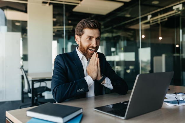 Excited businessman celebrating great news and luck looking at laptop screen in joy sitting in office interior