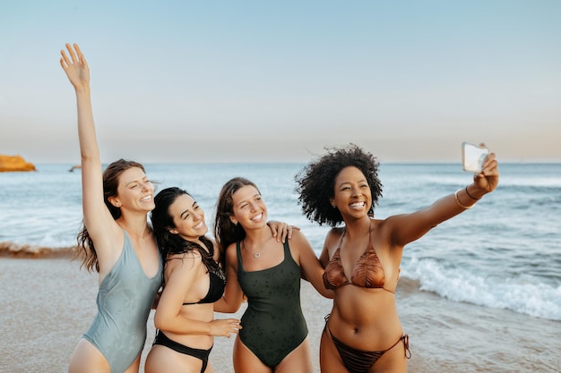 ワクワクした無心な多人種の女性 友達がビーチで一緒に過ごす瞬間を捕まえる