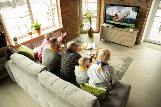 Excited caucasian family watching football, soccer sport match at home. Grandparents, parents and kid cheering for favourite national team. Concept of human emotions, support, togetherness.