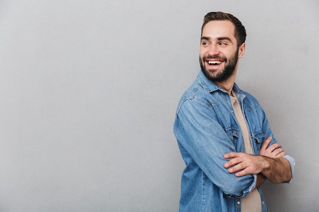 Excited cheerful man wearing shirt isolated over gray wall, arms folded, looking away