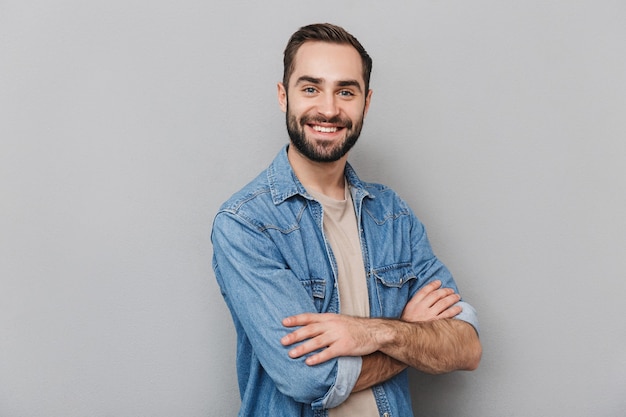 Excited cheerful man wearing shirt isolated over gray wall, arms folded