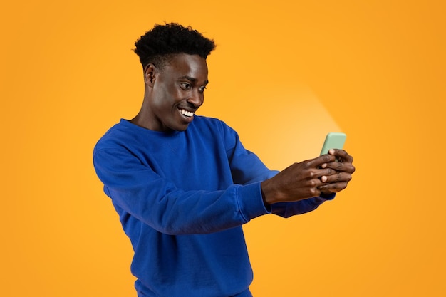 Excited cheerful young black guy looking at shining smartphone screen