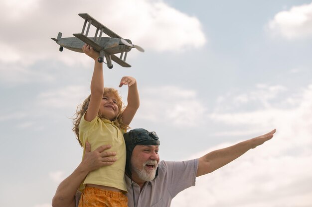 Excited child boy and grandfather having fun with plane outdoor on sky background with copy space ch...