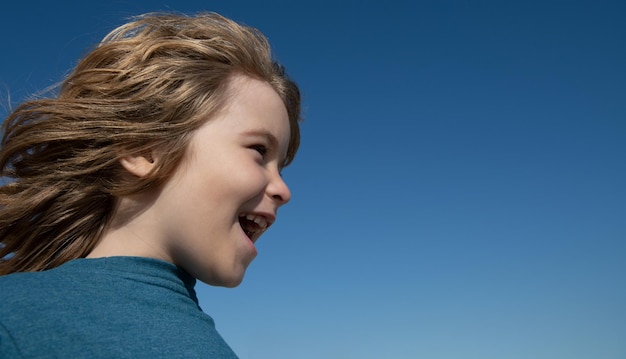 Excited child looking away and screaming on blue sky with copy space. Kids face, little boy portrait.